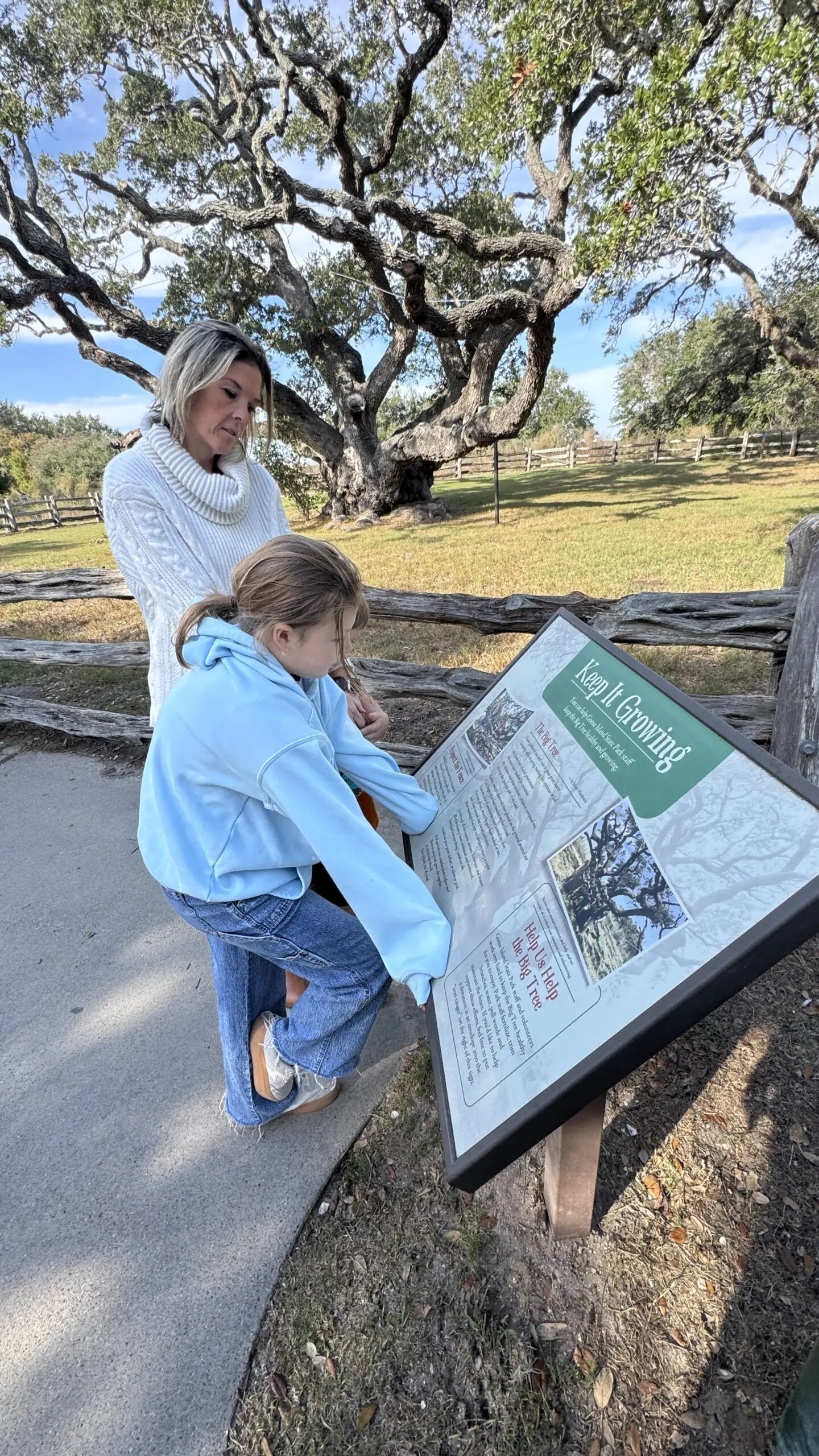 Mother and daughter reading a park interpretive sign under a large live oak tree