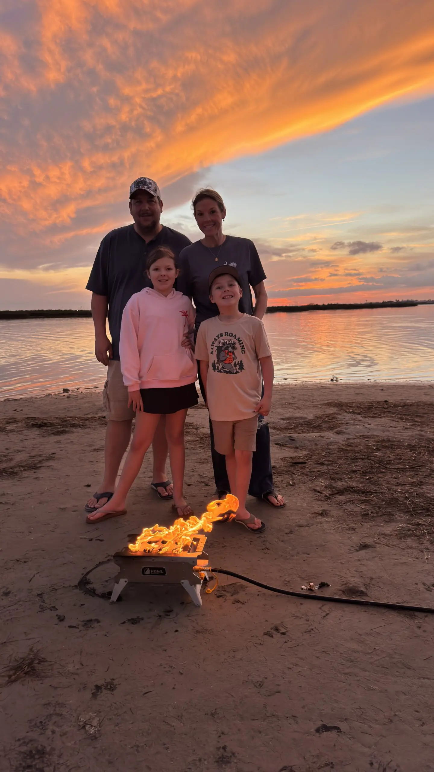 The Lawings family at a beach firepit at sunset with orange sky reflecting on the water