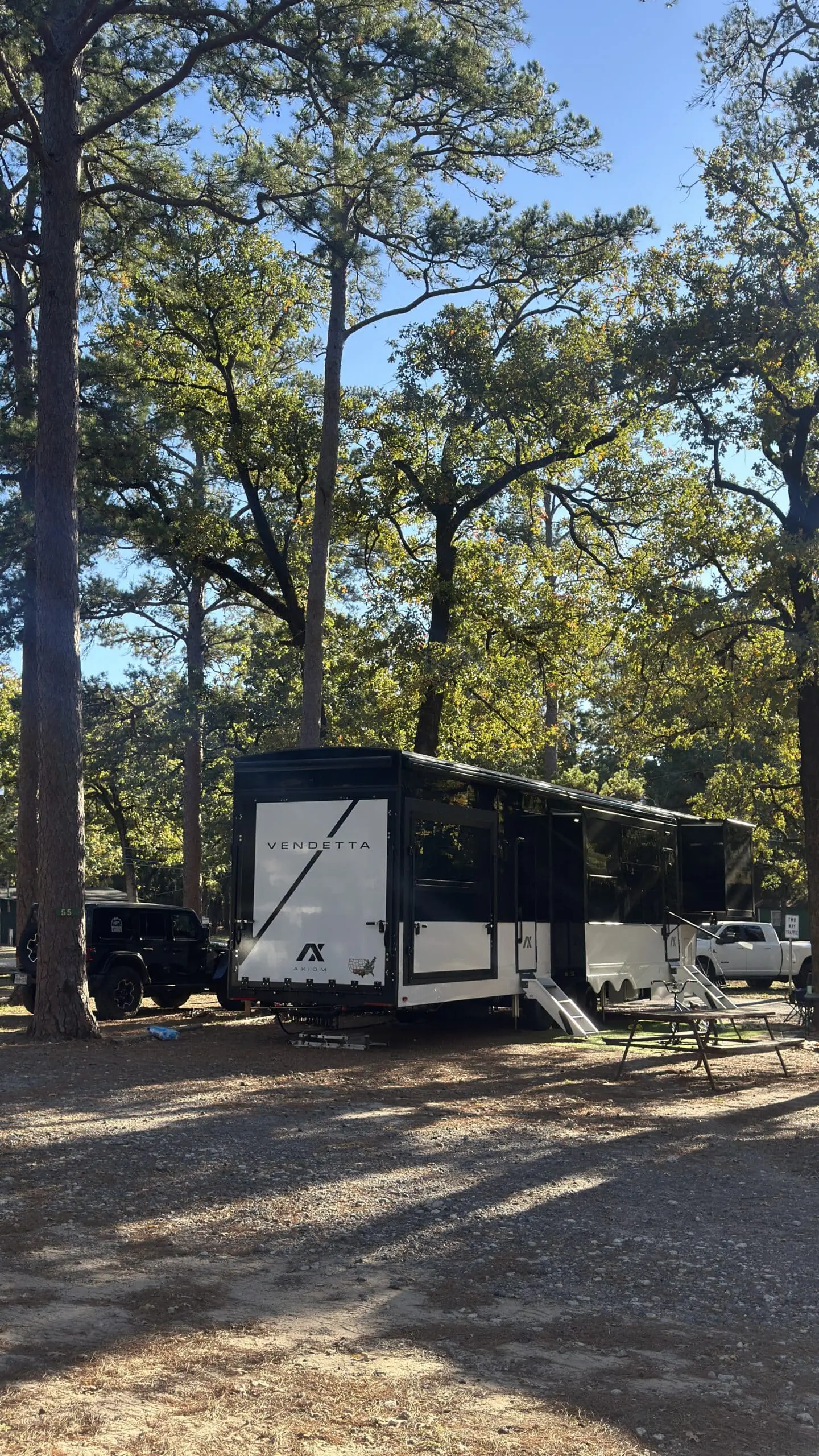 The Lawings Axiom Vendetta 4250 RV parked under tall pine trees at a campground